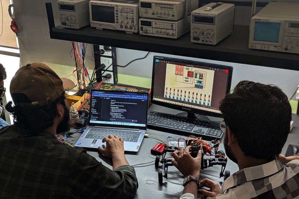 Students programming a robot arm at a lab bench with oscilloscopes